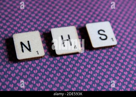 Alte getragene vintage Holztexturierte Würfel Schreibweise aus NHS, die British National Health Service, auf bunt gemusterten Hintergrund mit Platz für Kopie te Stockfoto