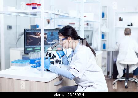 Experte in der Genetik, die Forschung mit Mikroskop, um chemische von menschlichen adn zu analysieren. Chemiker trägt Laborkittel mit moderner Technologie während wissenschaftlicher Experimente in steriler Umgebung. Stockfoto
