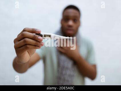 Kranker afrikanischer Mann, der Thermometer mit Fieber zeigt, grauer Hintergrund Stockfoto