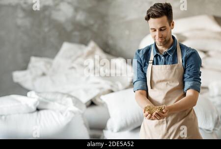 Lächelnder Brauereibesitzer oder Arbeiter in Schürze hält Weizen Oder Gerstenkörner in den Händen im Lager Stockfoto