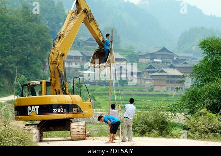 ZHAOXING DONG, CHINA - Juni 21, 2012: Chinesische Arbeiter Instandsetzung im freien Strom Kabel mit Bagger Kran. Miao Minderheit Dorf im Hintergrund Stockfoto