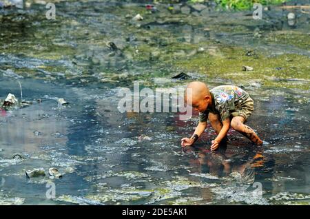 ZHAOXING DONG, CHINA - Juni 21, 2012: chinesischer Junge Kind spielen in Schwarz stagnierend, schlammigen Wasser in traditionellen Mioa Minderheit Dorf. Stockfoto