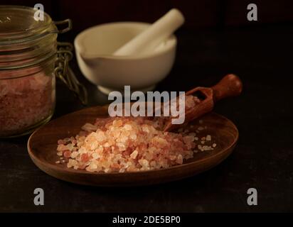 Himalayan rosa Salzkristalle in einer Holzschale, mit einem Mörser und Stößel und Glas Vorratsglas, England, Großbritannien, GB. Stockfoto