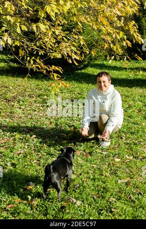 Schwarzer Mops Hund läuft zu seiner Geliebten mittleren Alters Frau in weißer Jacke auf natürlichem Hintergrund. Nahaufnahme. Speicherplatz kopieren Stockfoto