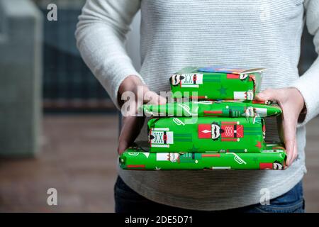 Eine Frau, die einen kleinen Stapel Weihnachtsgeschenke verpackt hält In bunt gefärbtem Weihnachts-Geschenkpapier Stockfoto
