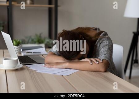 Erschöpfte unmotivierte junge Arbeiterin schlief am Tisch ein. Stockfoto