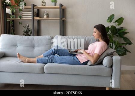 Junge arabische indische Frau auf dem Sofa mit Computer auf Runden liegen. Stockfoto