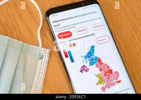 Geplante lokale Einschränkungen für Coronavirus Covid-19 in Großbritannien vom 2. Dezember 2020 auf einem Handy-Bildschirm mit Eine Gesichtsmaske im Hintergrund Stockfoto