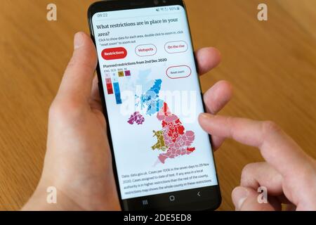 Karte der geplanten lokalen Beschränkungen des Coronavirus Covid-19 im Vereinigten Königreich Ab dem 2. Dezember 2020 auf einem Handy Der Bildschirm wird von der Hand einer Frau gehalten Stockfoto