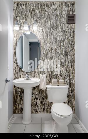 Ein kleines, tapeziertes Badezimmer mit einem weißen Standwaschbecken, das auf weißen Marmorfliesen sitzt. Stockfoto