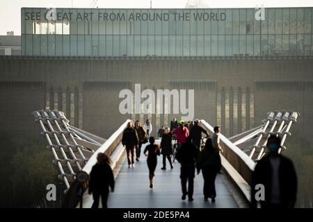 Menschen, die bei Sonnenuntergang über die Millennium Bridge gehen, mit der Tate Modern Gallery in London, England, Großbritannien, Europa Stockfoto