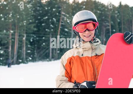 Portrait einer Snowboarderin mit Helm und Brille vor Wald und Hang. Stockfoto