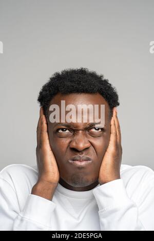 Nahaufnahme wütend verrückt gestresst afro Mann bedeckt seine Ohren und schaut nach oben, hört lästige laute Geräusche von oben Nachbarn isoliert auf Studio grau backgr Stockfoto