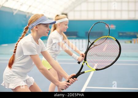 Zwei Mädchen im Teenageralter in aktiven, die mit ihren im Stadion stehen Beine in den Knien gebeugt und hält Tennisschläger bereit Drücken Sie den Ball während des Spiels Stockfoto
