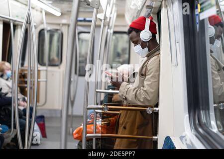 Afro-amerikanische Passagiermann stehen in U-Bahn-Zug, tragen Gesicht medizinische Maske, um sich vor Grippe-Virus, covid-19, Coronavirus, mit mobilen Phon zu schützen Stockfoto