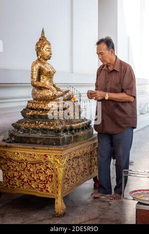 Thailand; Jan 2020: Buddhistischer Mann, der Goldblätter auf die goldene Buddha-Statue klebt, Mann, der in dankbarer Pose betet. Sitzender Buddha in Lotusposition. Wihan P Stockfoto