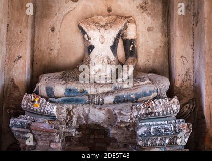 Alte Statue von Buddha, kopflos und armlos. Blumengirlande als Angebot neben dem linken Fuß. Zerstörte und zerbrochene Skulptur, antike Ruinen im Wat Chaiwat Stockfoto