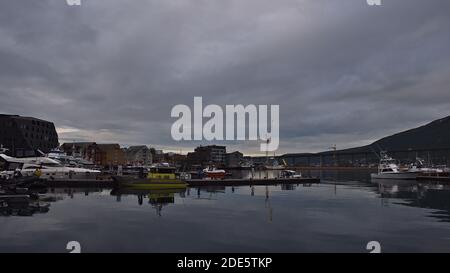 Tromsø, Norwegen - 08-23-2020: Friedlicher Hafen von Tromsø mit Anlegebooten und Anlegestelle spiegelt sich in der ruhigen Wasser- und Straßenbrücke Tromsøbrua. Stockfoto