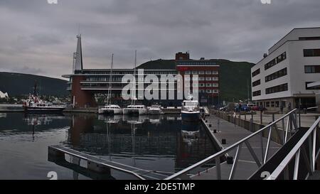 Tromsø, Norwegen - 08-23-2020: Hafen der norwegischen Stadt Tromsø mit Anlegestellen Boote in ruhigem Wasser und Hotel Scandic Ishavshotel (moderne Architektur). Stockfoto