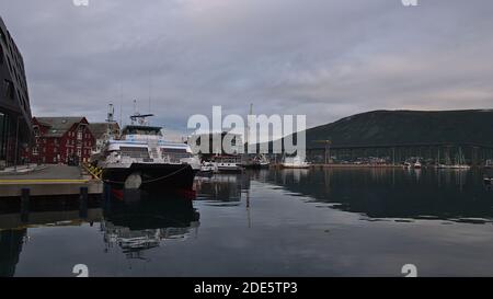 Tromsø, Norwegen - 08-23-2020: Ruhiger Hafen von Tromsø mit Anlegebooten und Straßenbrücke Tromsøbrua im Hintergrund an einem bewölkten Tag im Spätsommer. Stockfoto