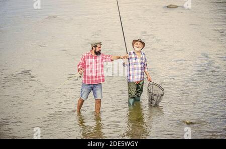 Arbeiten Sie im Team. Landurlaub. Hobby. Wilde Natur. Zwei glückliche Fischer mit Angelrute und Netz. Camping am Ufer des Sees, Vater und Sohn angeln. Wildern. Großes Spiel Angeln. Freundschaft. Stockfoto