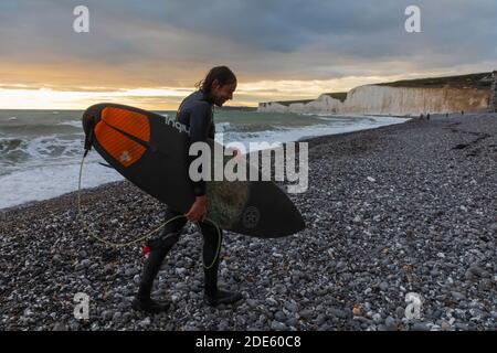 England, East Sussex, Eastbourne, Birling Gap, The Seven Sisters Cliffs and Beach, Male Surfer Walking on Beach mit Surfbrett Stockfoto