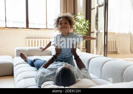 Lachende schwarze Pflegevater und adoptierten Sohn spielen auf dem Sofa Stockfoto