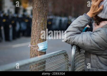 Frau, die ihren Kopf mit Gesichtsmaske hinter den Zaun hält Am Baum mit bewaffneter Polizei im Hintergrund befestigt Slowakische Anti-Regierungs-Demonstration Stockfoto