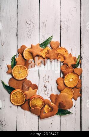 Weihnachtskranz aus Lebkuchen, gebackene Orangenscheiben, Mandarinenblätter auf der weißen Holztischoberfläche Draufsicht. Weihnachtsabend still-l Stockfoto