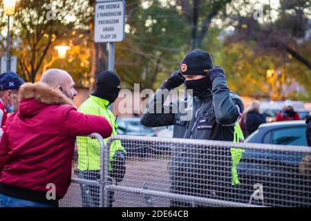 Männlicher Offizier in Schwarz im Gespräch mit Fremden hinter dem Zaun Zur Demonstration der slowakischen Anti-Regierungs-Regierung gegen die Beschränkungen des Corona-Virus Stockfoto