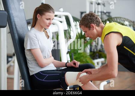 Fitnesstrainer wickelt Verband um das weibliche Knie. Stockfoto