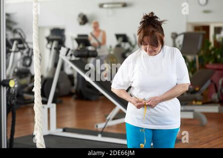 Reife kaukasische Frau Messung Taille im Fitnessstudio. Stockfoto