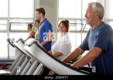 Ältere Frau, die auf dem Laufband läuft, lächelt der Kamera zu. Stockfoto