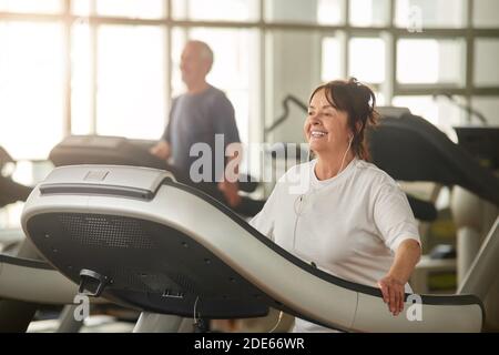 Positive ältere Frau, die auf dem Laufband läuft. Stockfoto