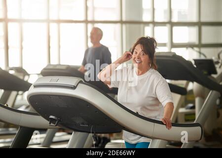 Aufgeregte ältere Frau auf dem Laufband im Fitnessstudio. Stockfoto