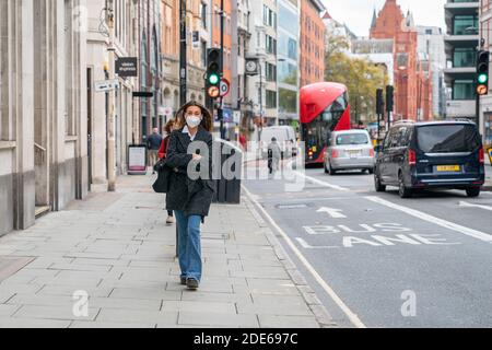 LONDON, ENGLAND - 23. Oktober 2020 - schöne schicke junge Brünette Frau, die mit einer Gesichtsmaske und gekleideter Mode durch High Holborn in London geht Stockfoto