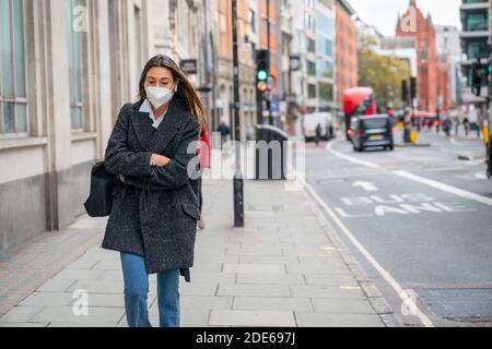 LONDON, ENGLAND - 23. Oktober 2020 - schöne schicke junge Brünette Frau, die mit einer Gesichtsmaske und gekleideter Mode durch High Holborn in London geht Stockfoto
