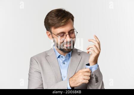 Nahaufnahme eines selbstbewussten Geschäftsmannes in einer Brille, der sich für das Büro anzieht, die Ärmel knöpft und lächelt und auf weißem Hintergrund steht Stockfoto