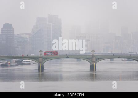 Nebliger Morgen in London mit rotem Londoner Bus über die Westminster Bridge. Silhouetten von neun Ulmen Turmblöcken. Skyline von London im Nebel. Themse Stockfoto