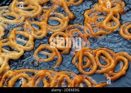 Jalebi-Teig in Öl braten. Roter und orangefarbener Teig wird für einen süßen Geschmack in Zuckersirup getaucht. Jalebi ist ein beliebter süßer Snack. Stockfoto