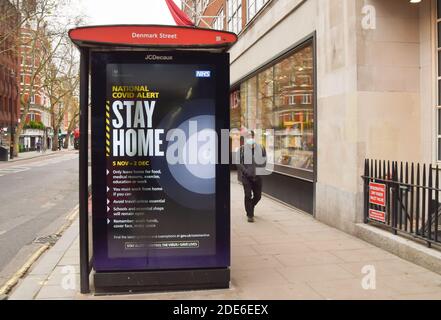 London, Großbritannien. November 2020. Ein Mann mit Gesichtsmaske als Vorsichtsmaßnahme gegen die Ausbreitung von covid-19 geht an einem Stay Home Schild an einer Bushaltestelle auf Charing Cross Road vorbei.England wird ein neues Tier-System durchsetzen, sobald die Sperre am 2. Dezember endet. Kredit: SOPA Images Limited/Alamy Live Nachrichten Stockfoto