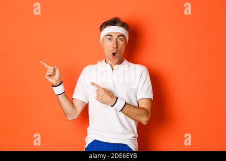 Portrait von überrascht Mann mittleren Alters Sport, zeigt etwas erstaunliches, zeigt Finger nach links und sieht fasziniert, tragen activewear für Stockfoto