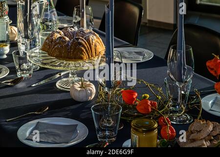 Ein mit Puderzucker bestäubter Bundt-Kuchen steht auf einem Glaskuchenständer inmitten herbstlicher Tischdekoration mit chinesischen Laternen-Phyllis und einem kleinen weißen Kürbis bei einer Ausgabe der Serie 'Kunst und Kochwerk' in Neuss, Deutschland. Ein Glas mit möglicherweise Senf oder Honig und geschnittenes Brot stehen in der Nähe bereit. Stockfoto