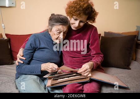 Positive alte Damen suchen Album Fotos Sofa zu Hause sitzen, fröhliche Freunde. Ältere Frau und ihre reife Krankenschwester beobachten Fotoalbum. Oma showi Stockfoto