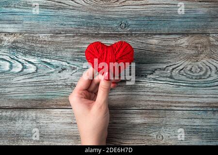 Ein rotes Herz in der Hand einer Frau über einem blau-grauen Holztisch. Stockfoto