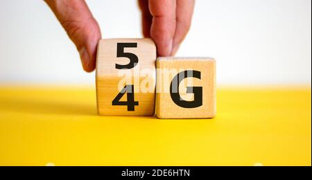 Zeit bis 5G. Männliche Hand dreht Holzblock und ändert Zeichen 4G auf 5G. Technologie, Netzwerk, Kommunikationskonzept. Schöner gelber Tisch. Weißer Hintergrund Stockfoto
