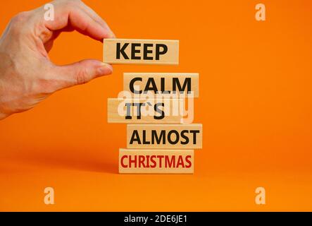 Weihnachtszeit. Männliche Hand platzieren Holzklötze mit den Worten "Keep Calm it is almost christmas". Schöner orangefarbener Hintergrund. Speicherplatz kopieren. Business und c Stockfoto