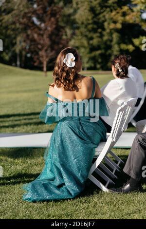 Wonan im smaragdgrünen Kleid und Blume in den Haaren sitzen auf dem Stuhl und warten auf Braut und Bräutigam. Ort der Hochzeitszeremonie Stockfoto