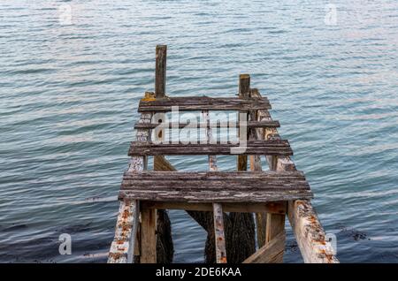 Ein alter hölzerner Steg oder Pier, der als Landungssteg dient Bühne im Meer für eine kleine Boa Stockfoto