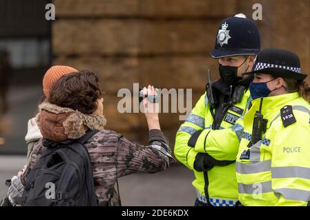 Weiße kaukasische weibliche videoing Polizisten auf einem COVID 19 Coronavirus Anti-Lockdown-protestmarsch in London, Großbritannien. Palmcorder Kamera Stockfoto